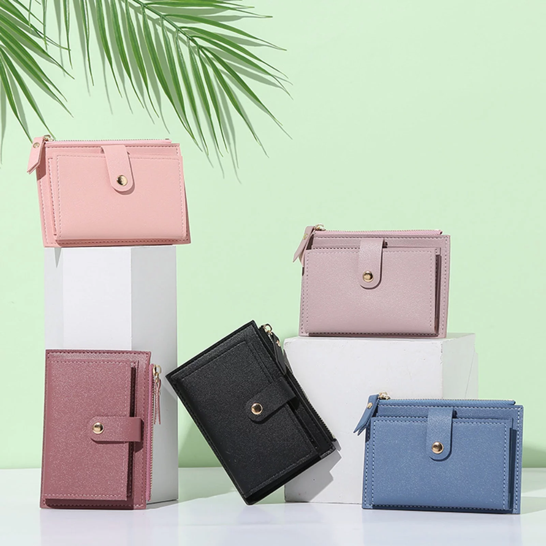Fünf Mini-Geldbörsen aus Leder in Rosa, Schwarz und Blau vor grünem Hintergrund.