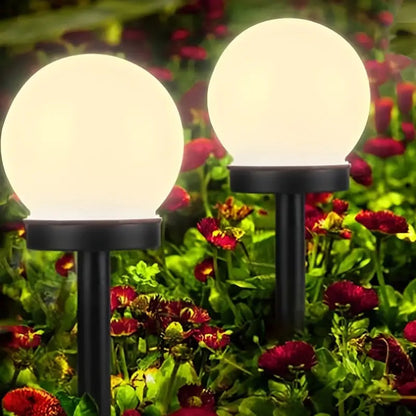 Zwei kugelförmige Solarleuchten im Garten, umgeben von roten Blumen, leuchten nachts.