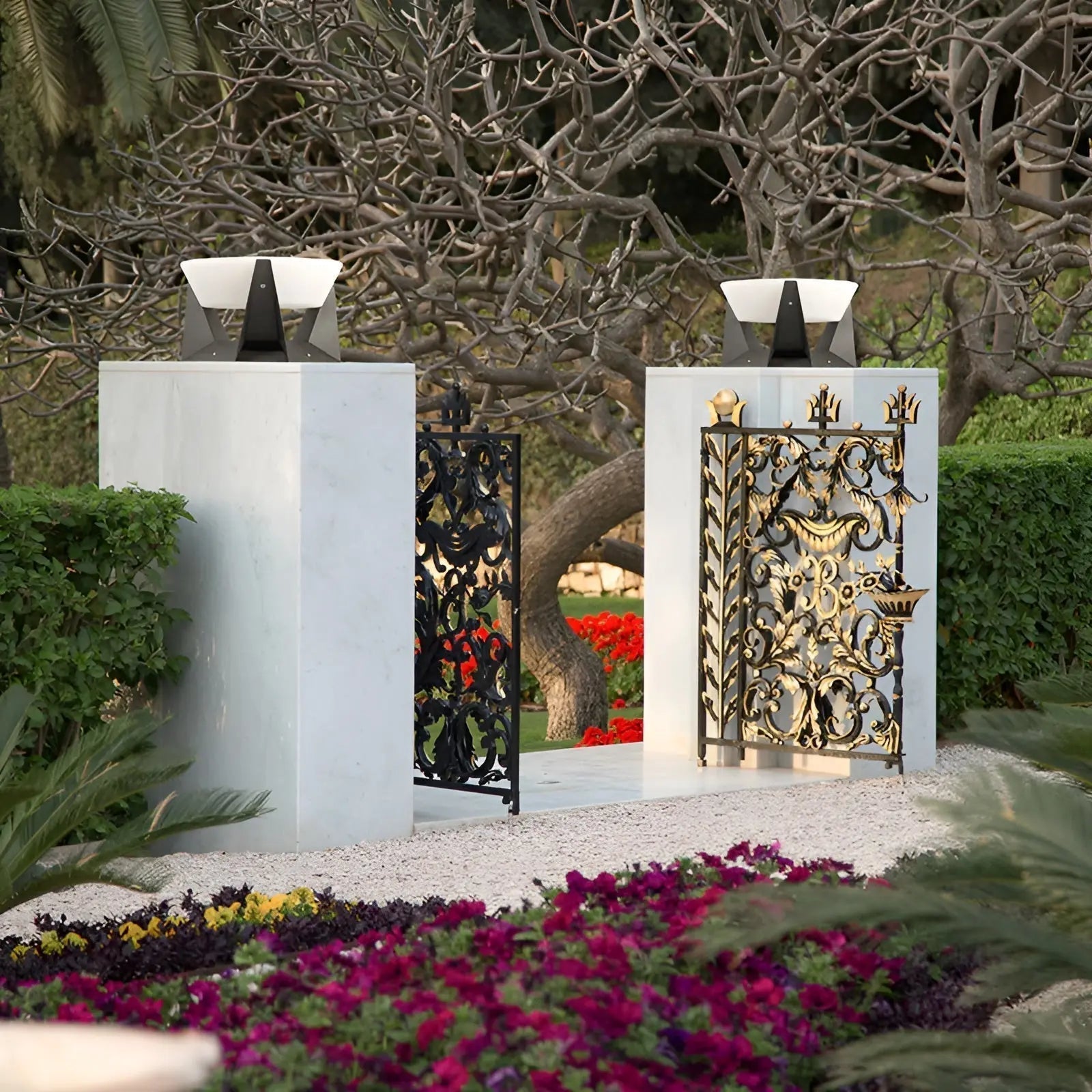 Dekoratives Gartentor aus Metall, schwarz und gold, mit floralen Mustern, umgeben von Blumen.