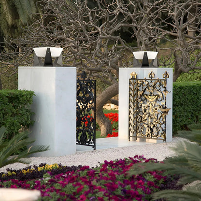 Dekoratives Gartentor aus Metall, schwarz und gold, mit floralen Mustern, umgeben von Blumen.