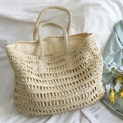 Beiger gehäkelter Strandtasche aus Stroh auf weißem Hintergrund mit Blumen und Zeitschrift.