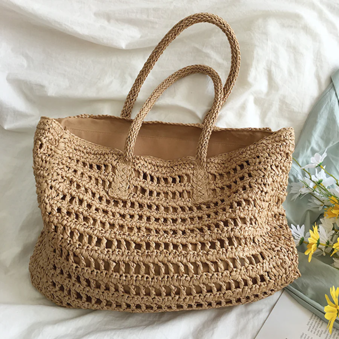 Beiger gehäkelter Strohtasche mit Griffen, ideal für Strand oder Einkauf, auf weißem Hintergrund.