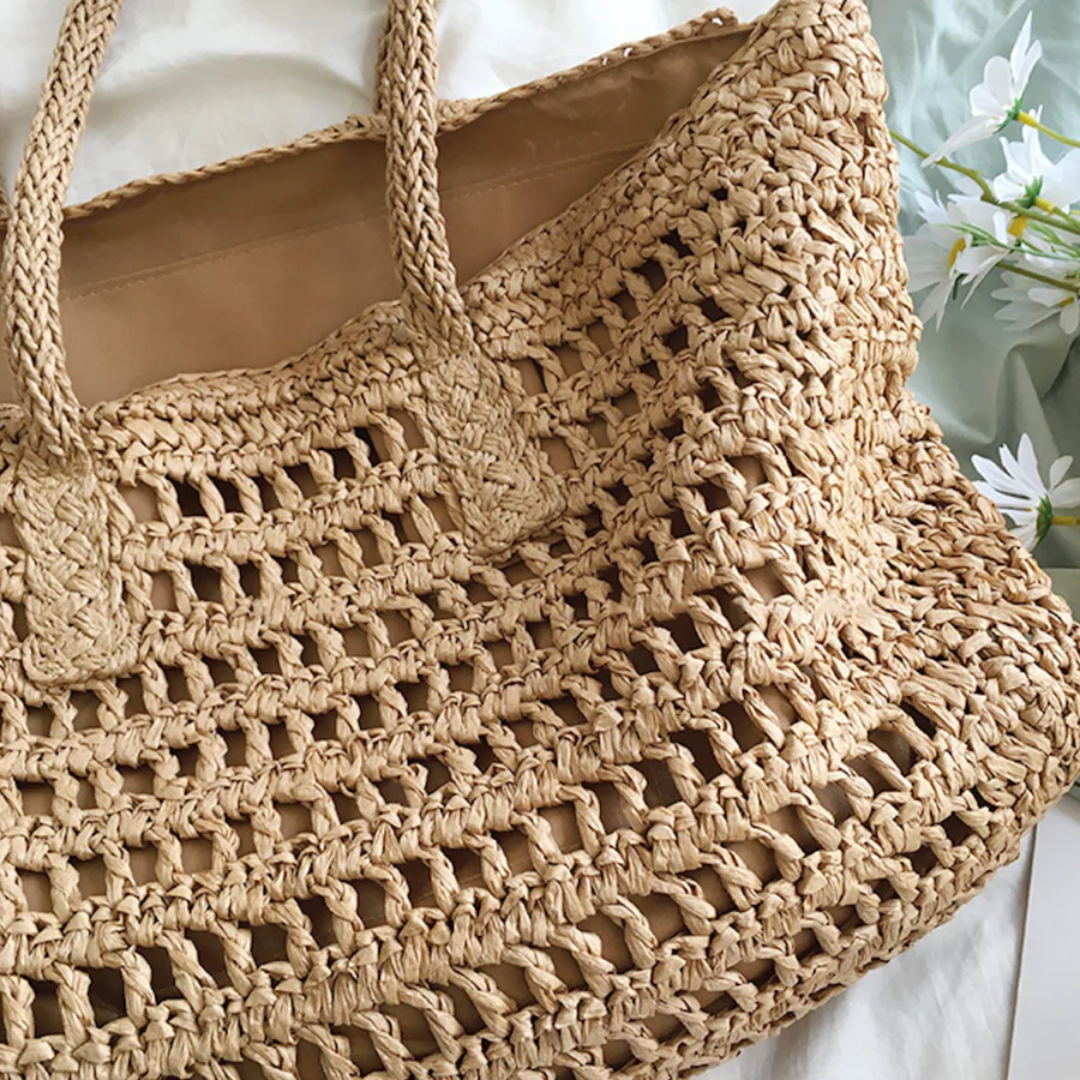 Geflochtene Strohtasche, beige, mit Henkeln, ideal für Sommer, Strand, Einkauf, umgeben von Blumen.