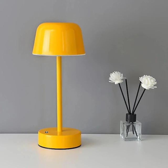 Gelbe Tischlampe aus Metall, modernes Design, neben Duftstäbchen auf weißem Tisch vor grauer Wand.