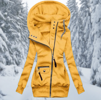 Gelber Damen-Wintermantel mit Kapuze, Reißverschluss, Taschen, vor verschneiter Waldkulisse.