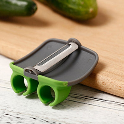 Grüner Gemüseschäler mit Doppelfingergriff auf Holzbrett, ideal für Gurken und Karotten.