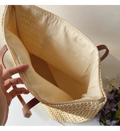 Geflochtene Strohtasche mit braunen Ledergriffen, beige Innenfutter, ideal für Sommerausflüge.