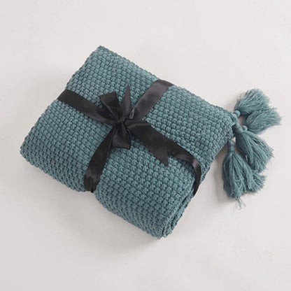 Gefaltete blaue Strickdecke mit schwarzen Schleifenband und Quasten, gemütliche Wohnaccessoires.