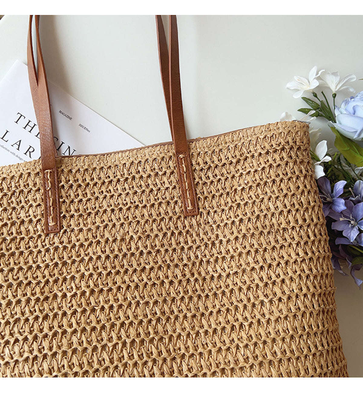 Geflochtene Strohtasche mit braunen Ledergriffen, Blumen und Zeitschrift, Sommermode Accessoire.