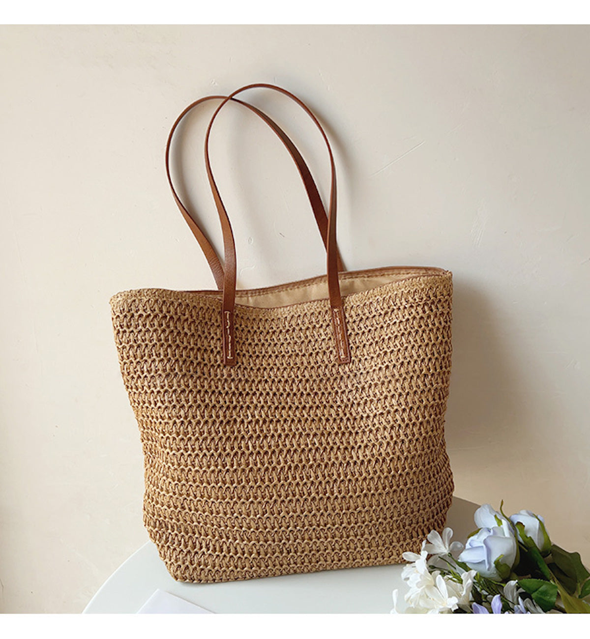 Geflochtene Strohtasche mit braunen Ledergriffen, ideal für den Sommer, auf weißem Tisch.
