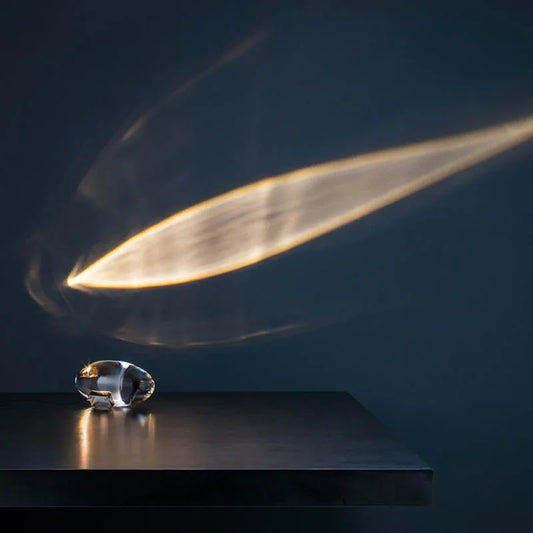 Kristallglas-Skulptur auf Tisch, reflektiert Lichtstrahl, modernes Design, dunkler Hintergrund.