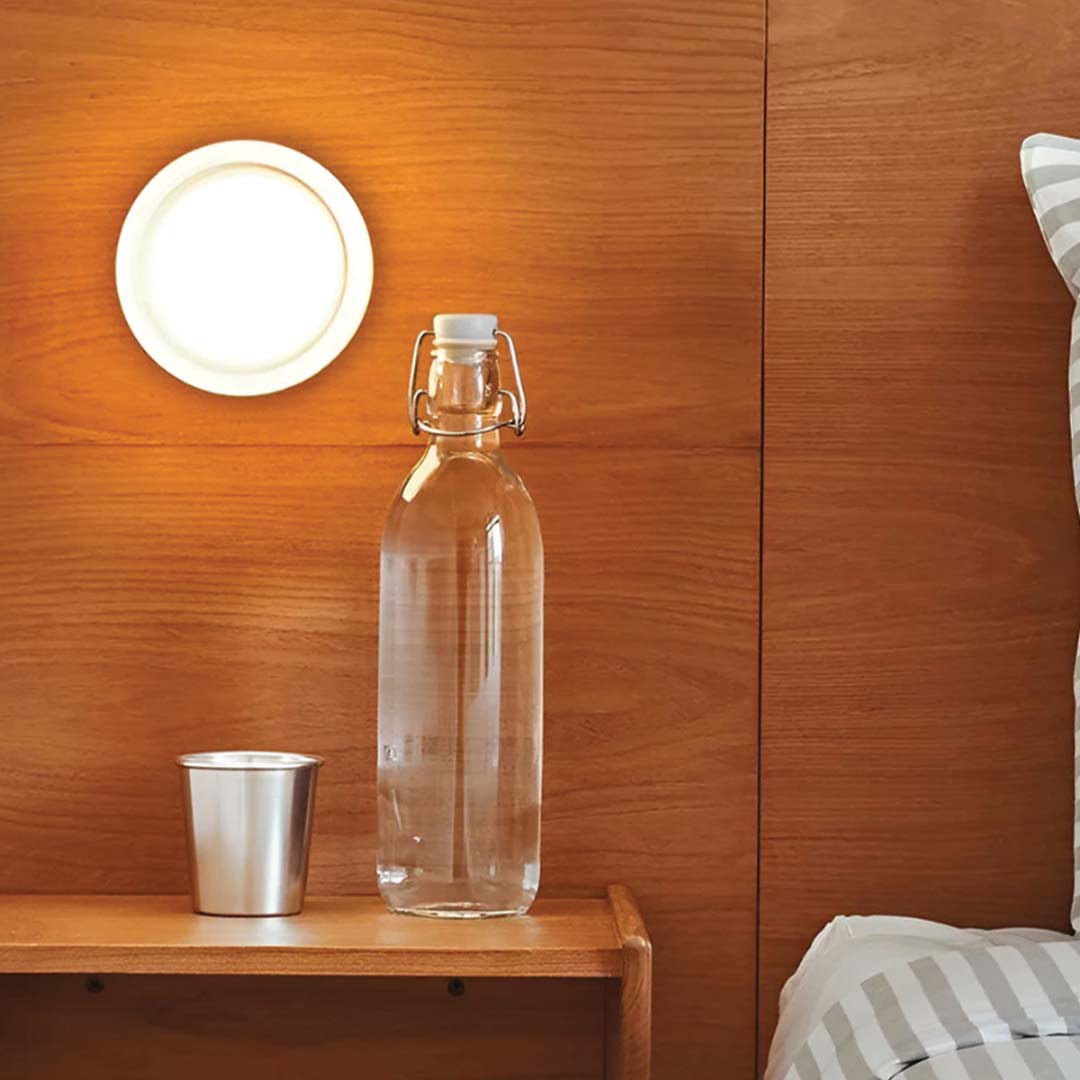 Glasflasche mit Bügelverschluss auf Holztisch, neben Metallbecher, vor Holzpaneelwand.