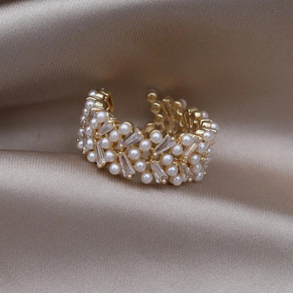 Goldener Ring mit Perlen und Kristallen auf beigem Stoff, eleganter Schmuck für Damen.