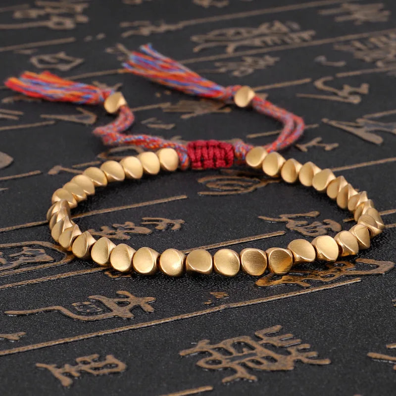 Goldenes Perlenarmband mit verstellbarem roten Kordelverschluss auf schwarzem Hintergrund.