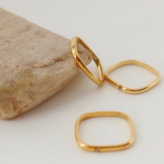 Drei goldene, quadratische Ringe auf hellem Hintergrund, minimalistisch, Schmuckdesign.