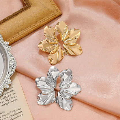 Goldene und silberne Blumen-Ohrringe auf rosa Seide, modische Accessoires, elegantes Design.