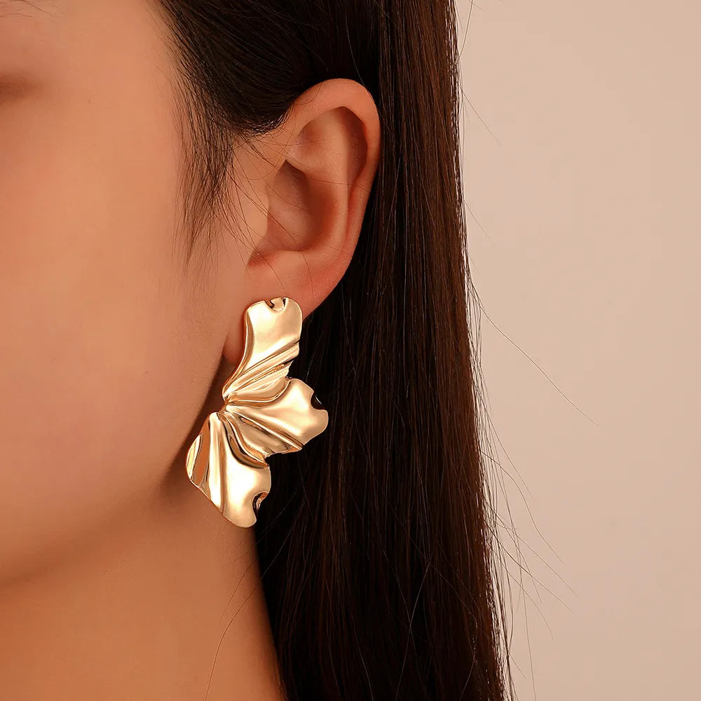 Goldene, blattförmige Ohrringe an Ohr, modisches Accessoire, eleganter Schmuck, Damenmode.