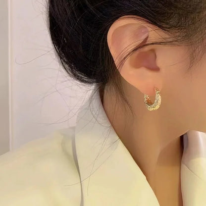 Goldene Creolen-Ohrringe, gehämmertes Design, getragen von Frau, eleganter Schmuck, Nahaufnahme.