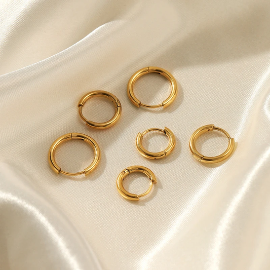 Goldene Creolen Ohrringe auf Seidenstoff, modischer Schmuck, elegantes Design, Damenaccessoire.