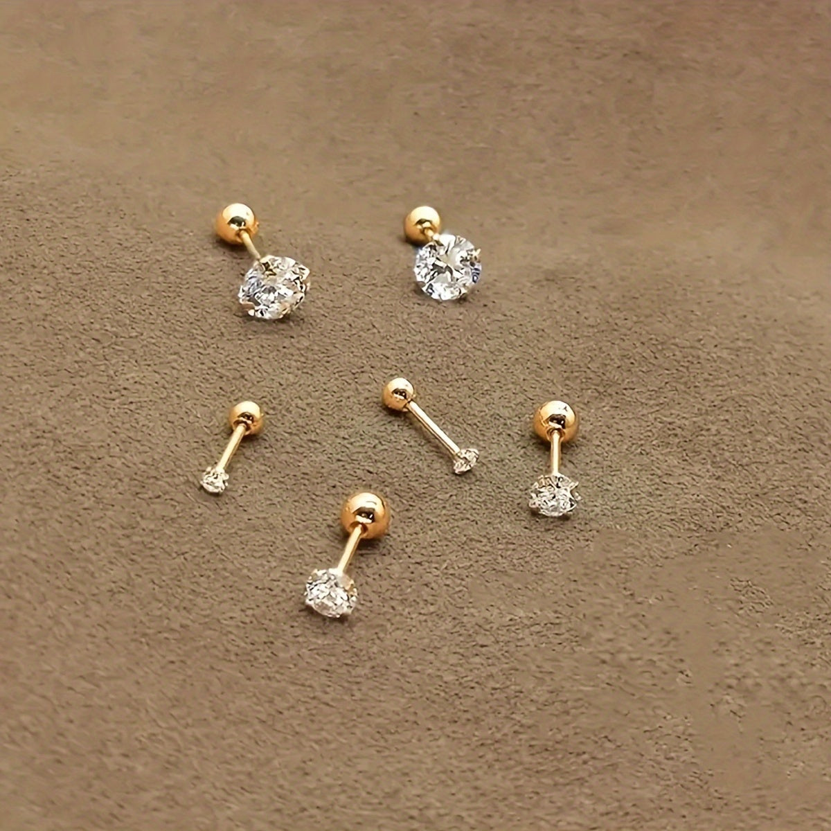 Goldene Ohrstecker mit Zirkonia auf beigem Hintergrund, eleganter Schmuck für Damen.
