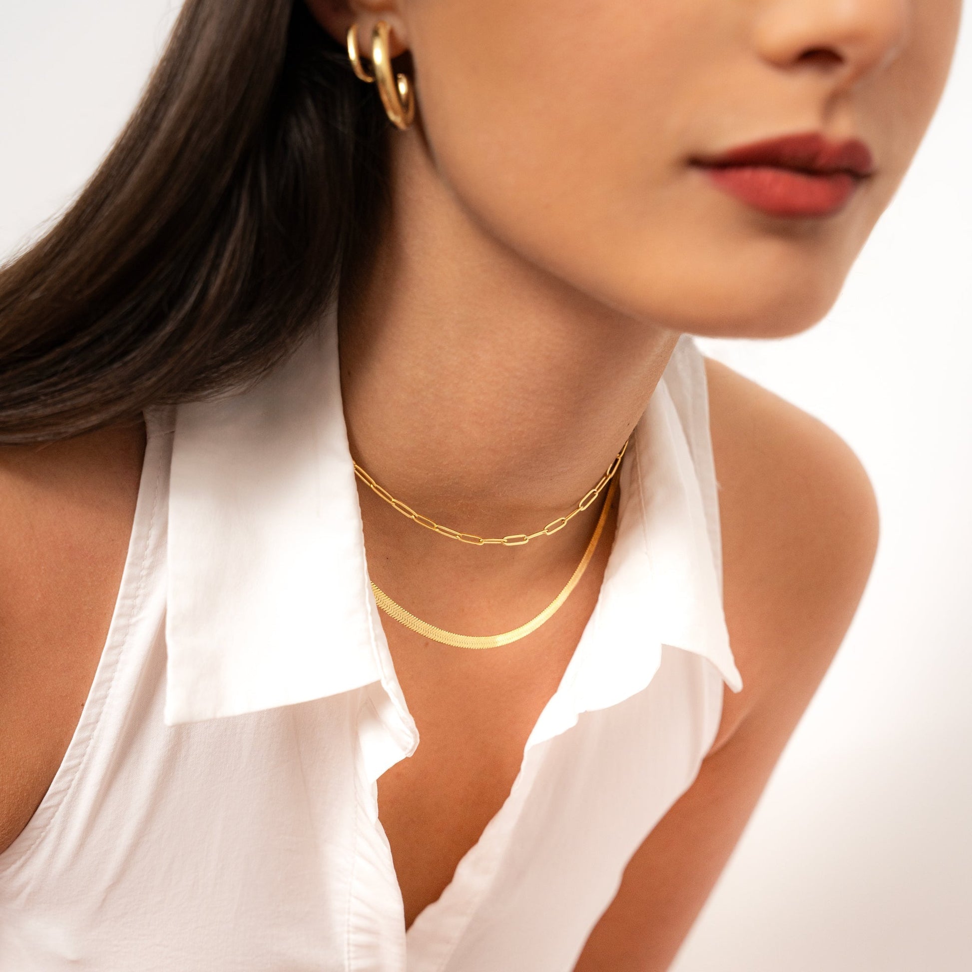 Frau mit goldener Halskette und Ohrringen, weißes Hemd, eleganter Schmuck, Modeaccessoires.