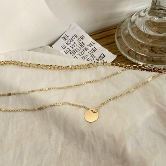 Goldene Halskette mit rundem Anhänger auf weißem Stoff, eleganter Schmuck, Damenaccessoire.