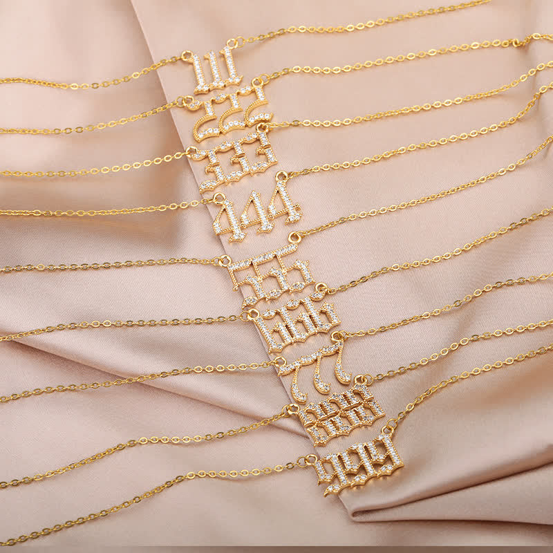 Goldene Armbänder mit Zahlenanhängern auf beigem Stoff, Schmuck, modisch, elegant.