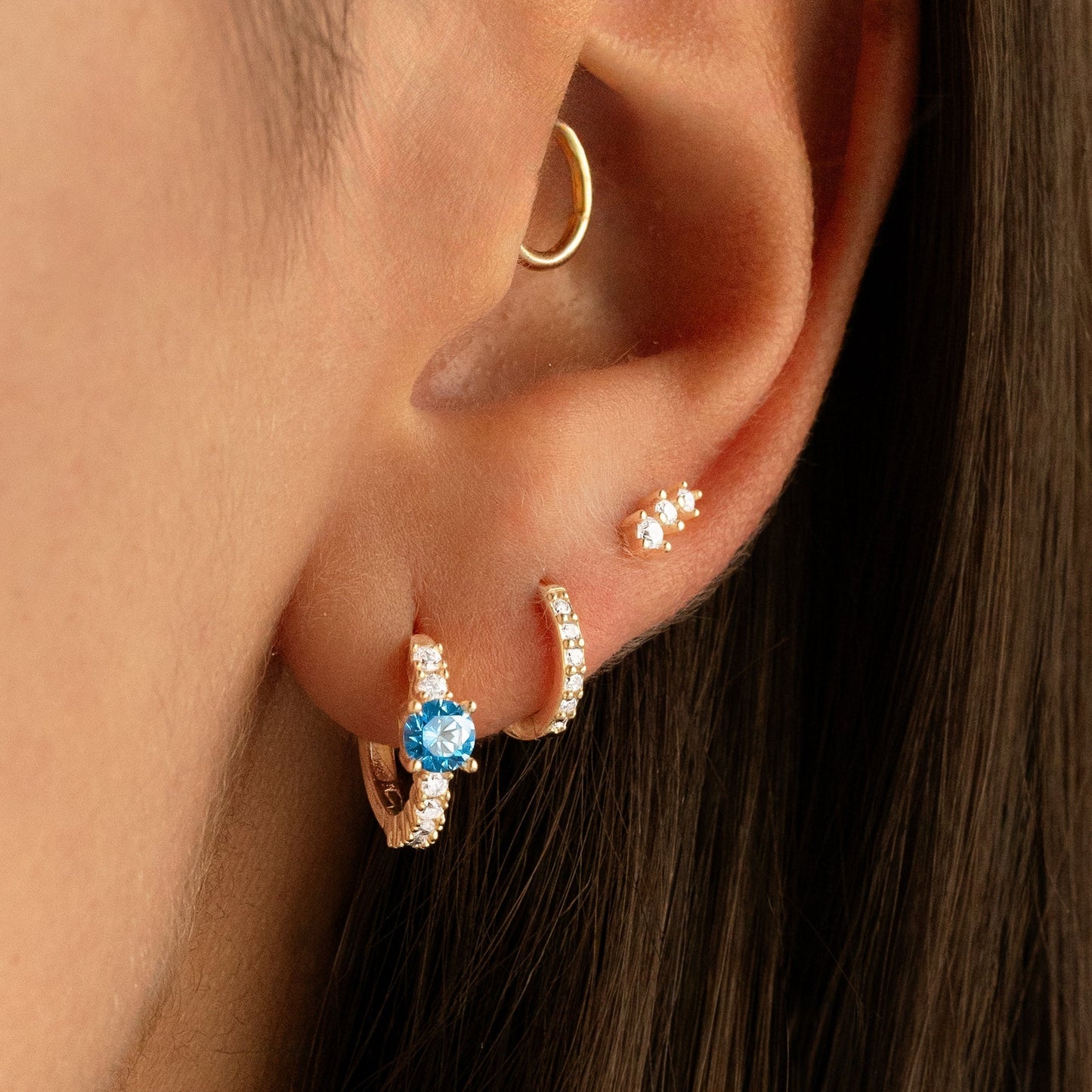 Nahaufnahme Ohr mit goldenen Creolen und blauem Stein, Ohrschmuck, modische Ohrringe.
