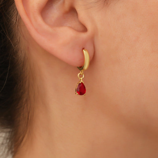 Goldener Ohrring mit rotem Tropfenanhänger, eleganter Schmuck, Nahaufnahme am Ohr.
