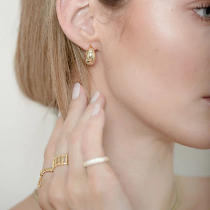 Frau mit goldenen Ohrringen und Ringen, Nahaufnahme, Schmuck, Modeaccessoires, elegantes Design.