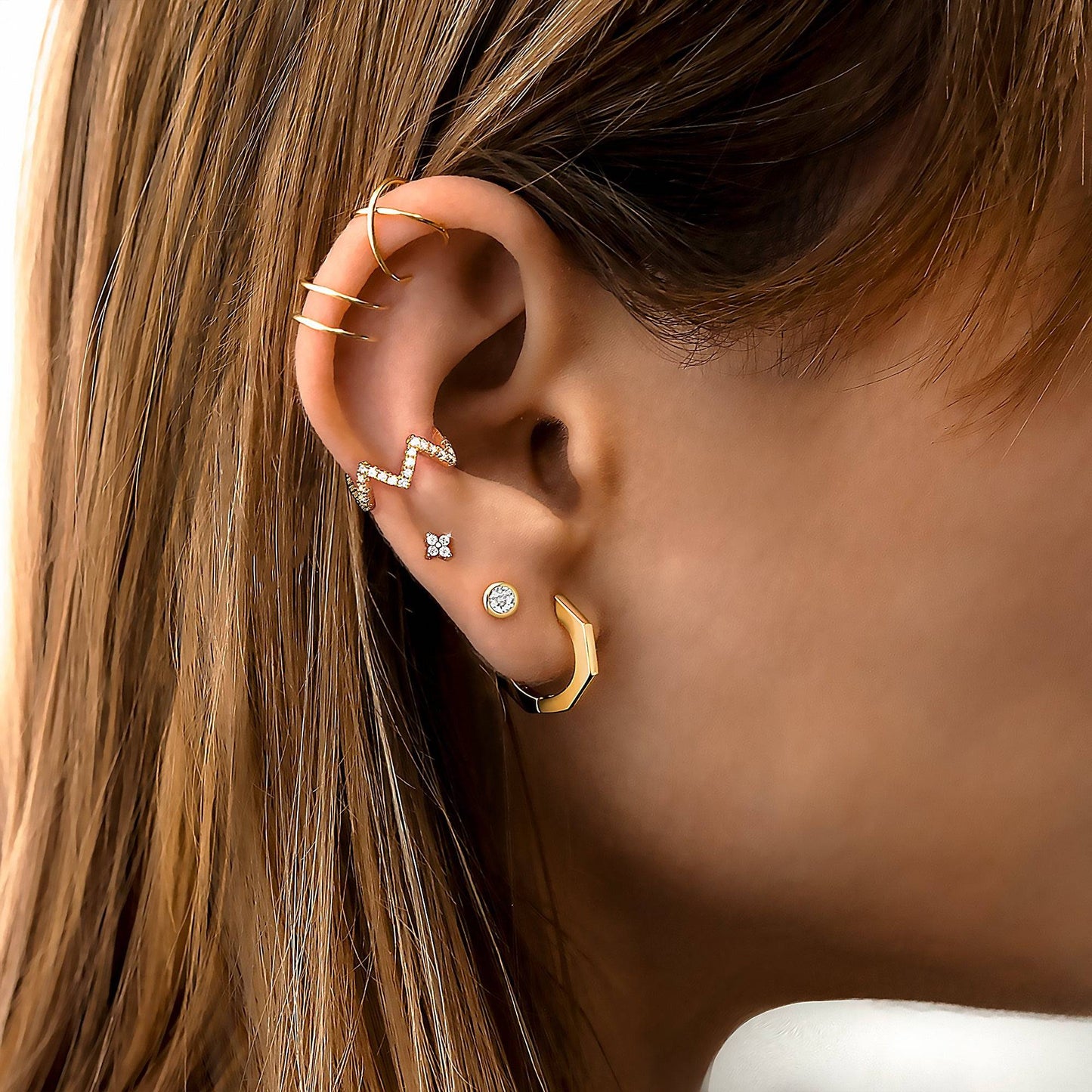 Frauenohr mit goldenen und silbernen Ohrringen, Zickzack-Design, Schmuck, modisch, elegant.
