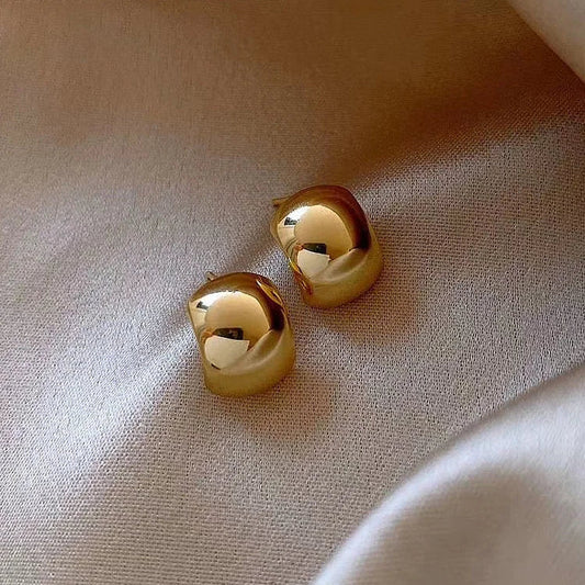 Goldene, glänzende Ohrringe auf beigem Stoff, eleganter Schmuck, modisches Accessoire.