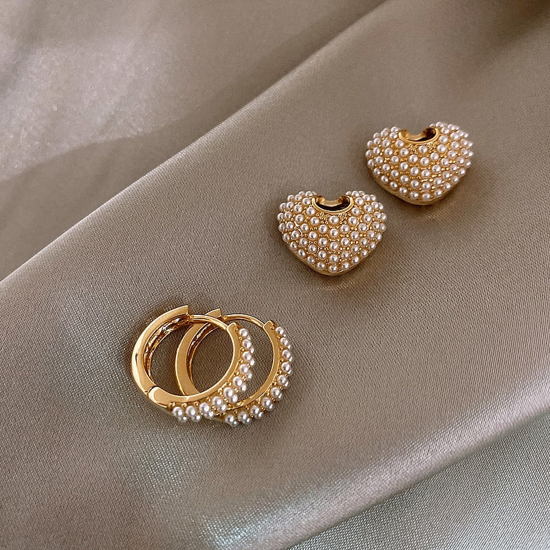 Goldene Ohrringe mit Perlen, Herzform und Creolen, eleganter Schmuck auf Seidenstoff.