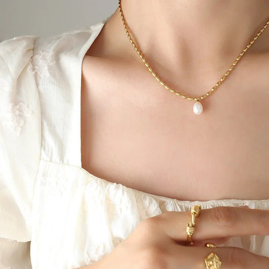 Frau mit goldener Halskette und Perlenanhänger, weiße Bluse, goldene Ringe.