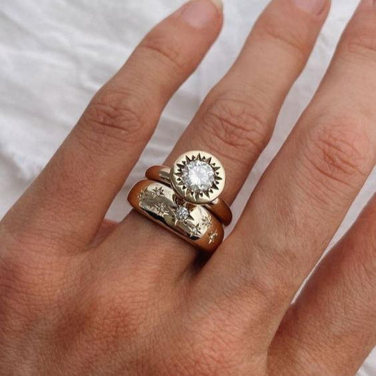 Damenhand mit drei goldenen Ringen, einer mit großem Diamant, auf weißem Hintergrund.