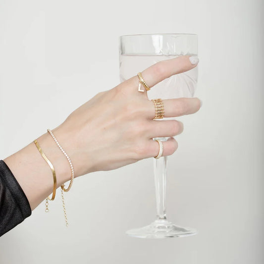 Hand mit goldenen Ringen und Armbändern hält Weinglas, Schmuck, Modeaccessoires, elegantes Design.