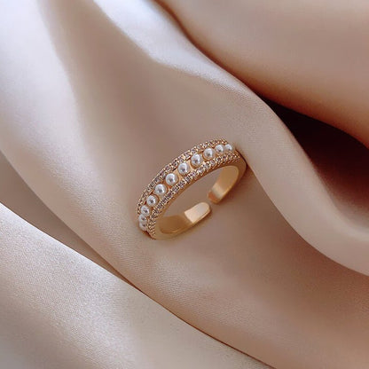 Goldener Ring mit Perlen und Strasssteinen auf beigem Stoff, eleganter Schmuck, Damenaccessoire.