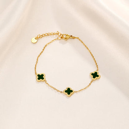 Goldenes Armband mit grünen Kleeblatt-Anhängern auf cremefarbenem Hintergrund.