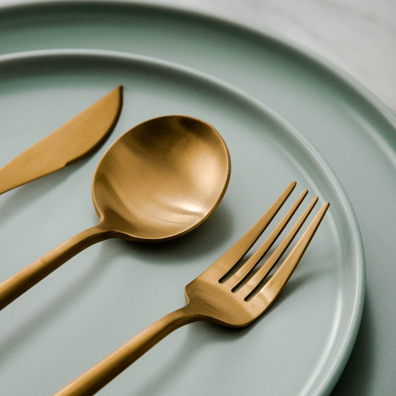 Goldenes Besteck-Set auf mintgrünem Teller, modernes Design, Edelstahl, Essbesteck.