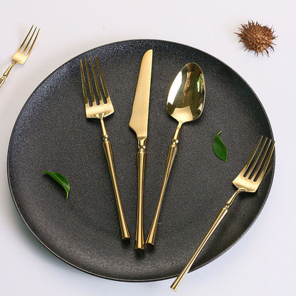 Goldenes Besteckset auf schwarzem Teller, bestehend aus Gabel, Messer, Löffel, elegant, modern.