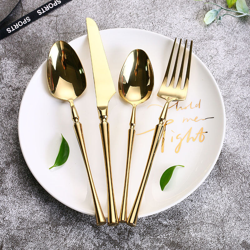 Goldenes Besteckset auf weißem Teller, bestehend aus Messer, Gabel, Löffel und Teelöffel.