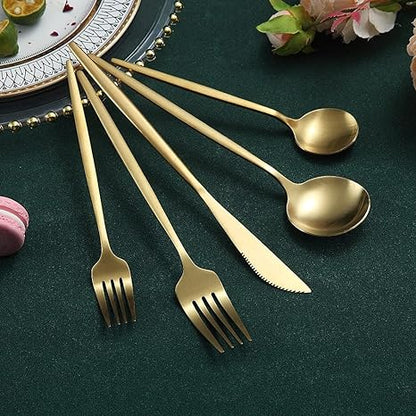 Goldenes Besteckset aus Edelstahl, bestehend aus Gabeln, Löffeln und Messer auf grünem Tuch.