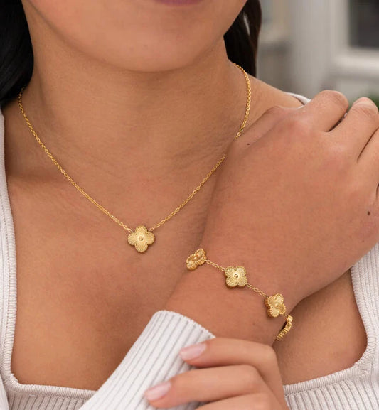Frau trägt goldene Halskette und Armband mit Blumenanhänger, eleganter Schmuck, Nahaufnahme.