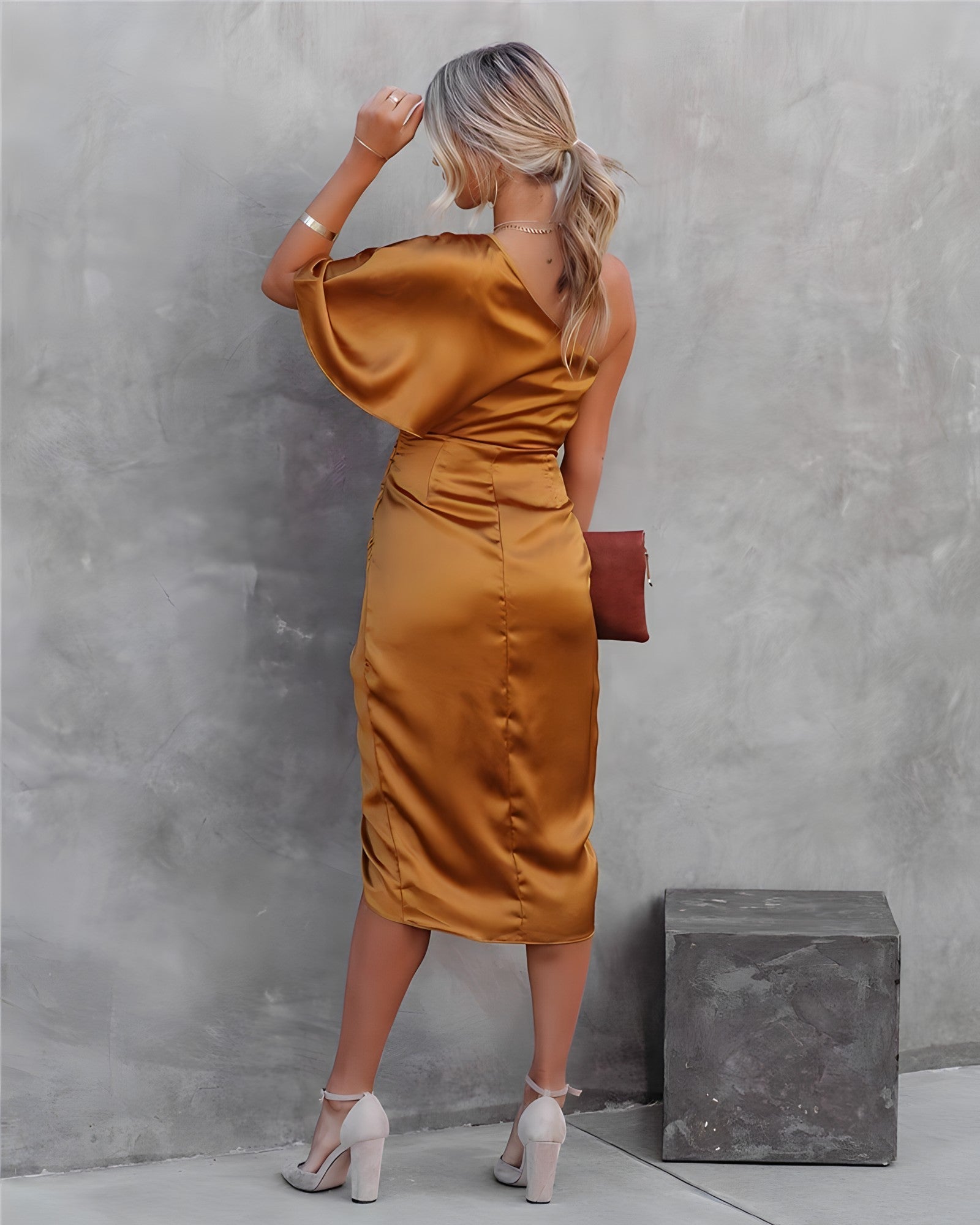 Frau in goldfarbenem Satin-Kleid, schulterfrei, mit Clutch, elegante Abendmode.