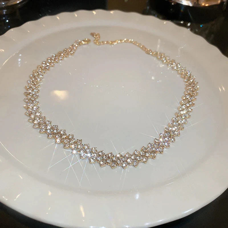 Goldene Halskette mit funkelnden Kristallen auf weißem Teller, eleganter Schmuck für Damen.