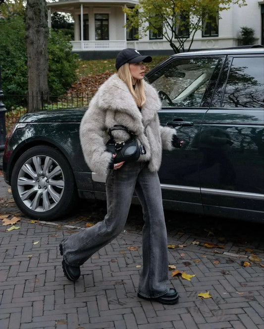 Frau in grauem Kunstpelzmantel und Jeans vor grünem SUV, Herbstszene, modisch, urban.