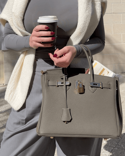 Frau mit grauer Lederhandtasche, Kaffeebecher und Zeitschrift, modisch, elegant, draußen.