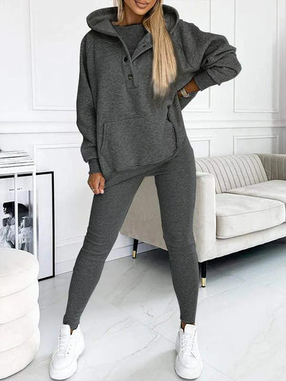 Frau in grauem Jumpsuit mit Kapuze, lässig, bequem, modisch, Wohnzimmer, weiße Sneaker.