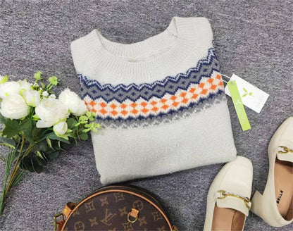 Grauer Strickpullover mit buntem Muster, weiße Blumen, braune Tasche, weiße Schuhe.