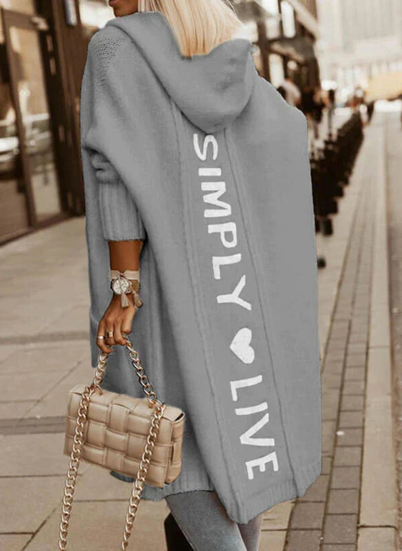 Frau in grauem Kapuzenmantel mit "Simply Live"-Aufdruck, beige Tasche, Stadtstraße.